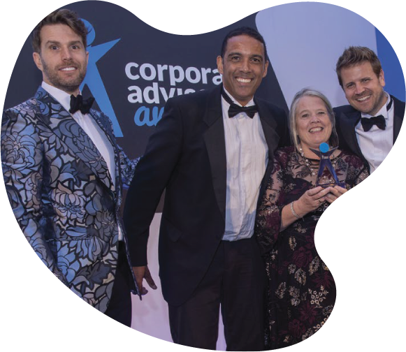 Four people dressed in formal attire pose together, holding an award at a corporate event. The backdrop features the text 